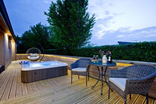 a deck with a hot tub and two chairs and a table at Orchard Lodge, Strawberryfield Park in Cheddar
