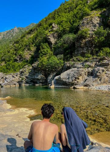 two people sitting on the beach looking at a body of water at Hostel 90pods & C O working in Shkodër