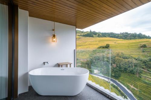 a bath tub in a bathroom with a large window at Longji Vista Retreat--Panoramic View of Terrace, Sunrise ,Heated Pool & Affordable Luxury in Longsheng