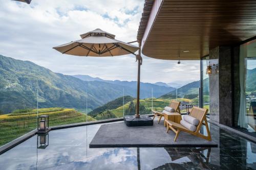 a balcony with chairs and an umbrella and mountains at Longji Vista Retreat--Panoramic View of Terrace, Sunrise ,Heated Pool & Affordable Luxury in Longsheng