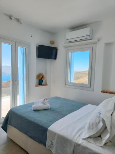 a white bedroom with a bed with two windows at Villa Manesi in Kithnos