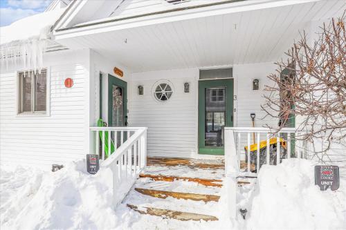 a white house with a green door in the snow at Riverside Getaway in Stowe