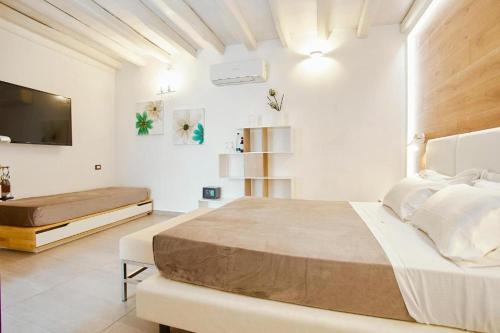 a white bedroom with a large bed and a flat screen tv at Hotel La Tavernetta in Scopello