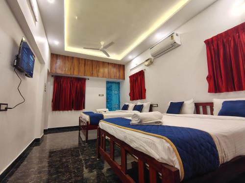 two beds in a room with red curtains and a tv at THE VILLA Pondicherry in Puducherry
