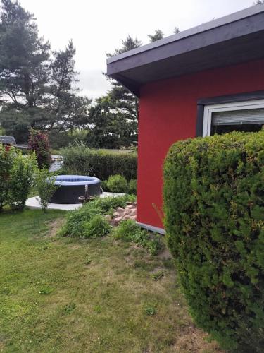 a red house with a bush next to a yard at Ferienbungalow in Zirkow