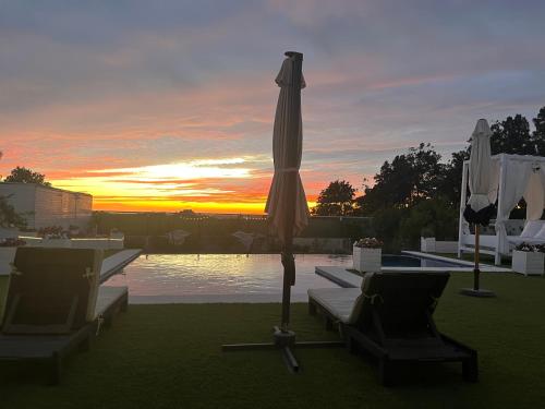 an umbrella and two chairs and a pool with the sunset at Puesta de Sol Doñana Adults Only in Sanlúcar de Barrameda