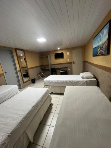 a hotel room with three beds and a tv at Hotel Veraneio in Recife