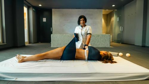 a woman laying on a bed as a woman is getting her hair cut at Altafiumara Resort & Spa in Villa San Giovanni
