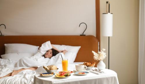 a woman laying in bed with a tray of food at Five Seas Cannes, a Member of Design Hotels™ in Cannes
