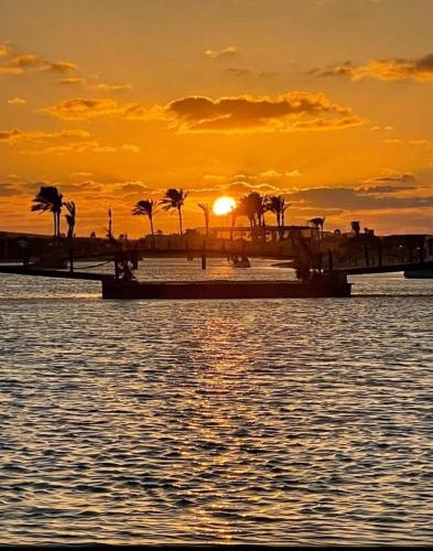 a sunset over the water with a bridge and palm trees at The Red Residence North Coast Egypt in Mājid Abū Zayd