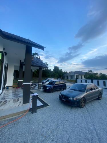two cars parked in a parking lot next to a house at Permai Homestay in Kampong Burok