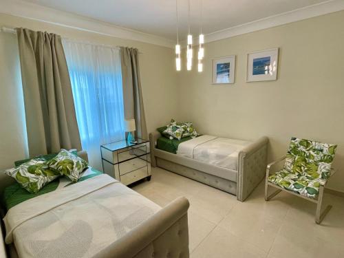 a bedroom with two beds and a chair and a window at Eden Caribe Deluxe 2BR Apartment - Bavaro Beach Escape in Punta Cana