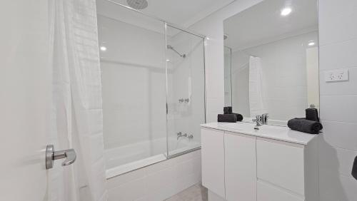 a white bathroom with a shower and a sink at Pelican Shore Villa 2 - Kalbarri WA in Kalbarri