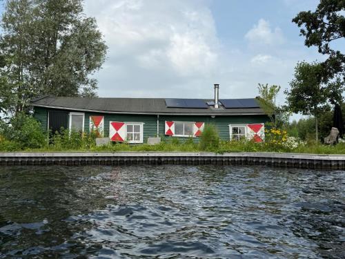 a green house with a solar roof next to a body of water at The Historical Trick Hut in the middle of the Lake in Baambrugse Zuwe