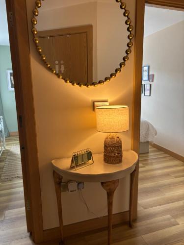 a table with a lamp and a mirror on a wall at Cosy central hideout in Ware