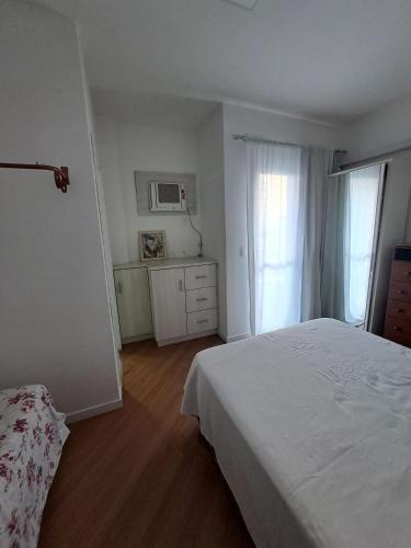 a white bedroom with a bed and a window at Apartamento no Centro de Brusque/SC in Brusque