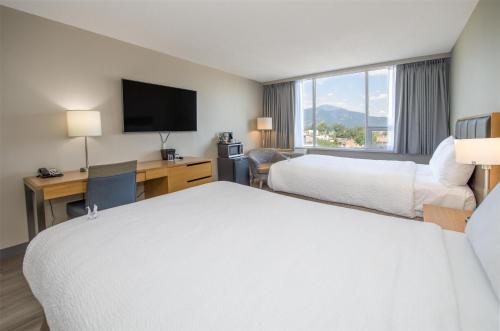 a hotel room with two beds and a desk and a television at Coast Chilliwack Hotel by APA in Chilliwack