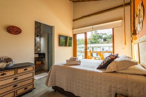 a bedroom with a bed with a dresser and a window at Barlavento Villas Chalés e Suites in Ilhabela