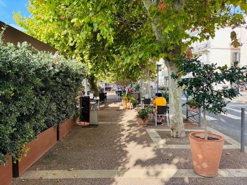 a sidewalk with trees and people sitting at tables at Golfe-Juan Gem, Pool & Beach in Vallauris