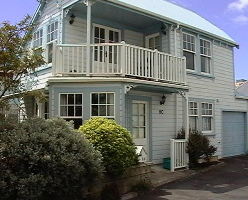 a white house with a balcony on top of it at Gorgeous cottage near hospital, with garage in Wellington