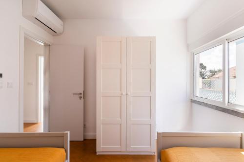 a white bedroom with two beds and a window at Lazy Point Caparica in Costa da Caparica