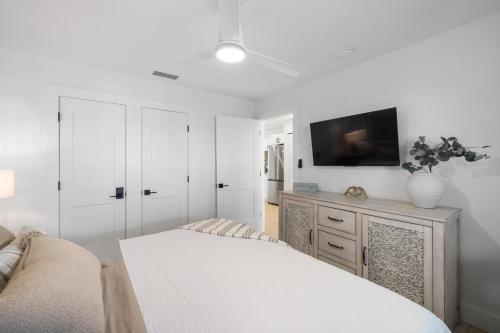 a white bedroom with a bed and a flat screen tv at Heat of Siesta Village Walk to Beach w heated Pool in Siesta Key
