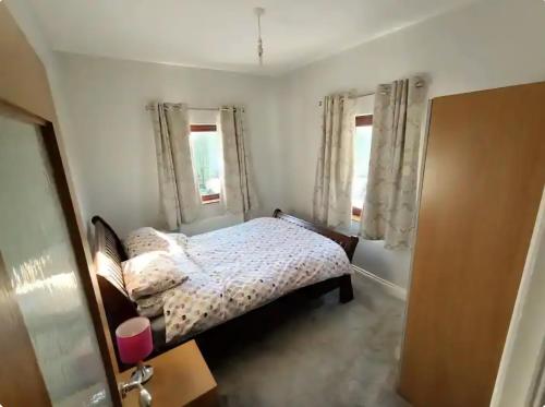 a small bedroom with a bed and two windows at Orchard Brooke Cottage in Downpatrick