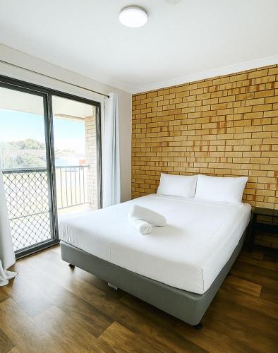 a bedroom with a large white bed with a brick wall at Waves Geraldton in Geraldton