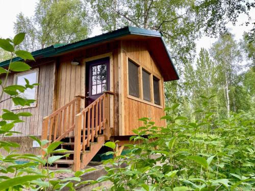 a wooden cabin in the woods with a porch at Talkeetna Wilderness Lodge & Cabin Rentals in Sunshine