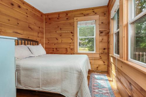 a bed in a room with wooden walls and windows at Maine Coastal Cottage in Wells