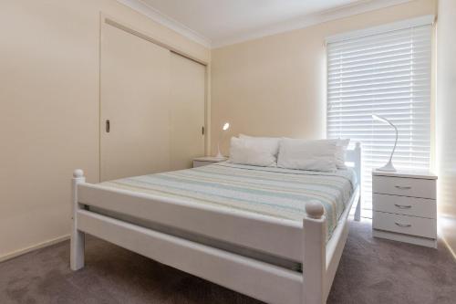 a white bedroom with a bed and a window at Amaroo Sunset Lodge in Smiths Lake