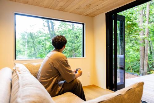 a man sitting on a couch looking out a window at Morinest 北軽井沢 in Tsumagoi
