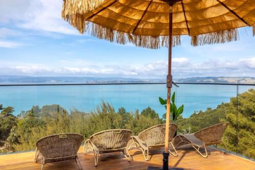 a patio with chairs and an umbrella and the ocean at Woodside Bay Estate in Waiheke Island