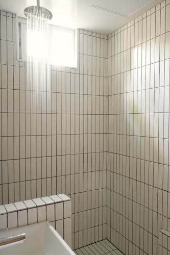 a white tiled bathroom with a tub and a window at Pyoseon Mansion in Seogwipo