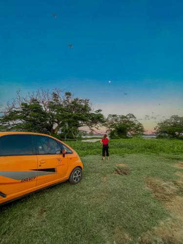 a person standing next to a car parked in a field at Nehansa Resort and safari in Tissamaharama