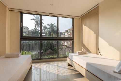two beds in a room with a large window at Luxury 2BHK Apartment Near Candolim Beach in Candolim