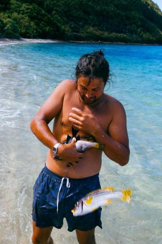 a man holding a fish in the water on the beach at Tai Evi in Soso