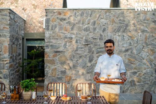 a man holding a tray of food on a table at StayVista at The Stone Age Home with Pool, Lawn, BBQ & Bonfire in Jaipur