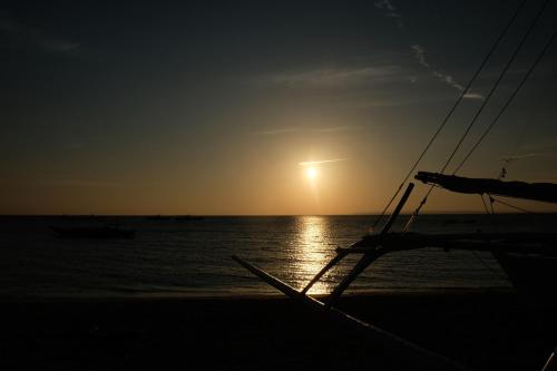 a boat on the beach with the sun in the sky at Skott's Comfy Lodge in Bantayan Island