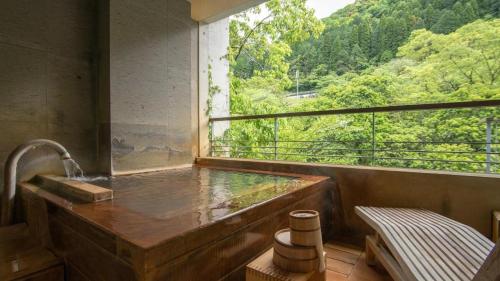 a bath tub with a window with a view of a forest at Myoken Ishiharaso in Kirishima