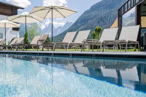 a hotel swimming pool with chairs and umbrellas at Alpenwellnesshotel St. Veit in Sesto