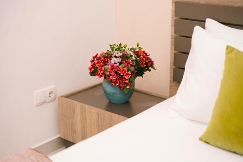 a blue vase with red flowers on a table next to a bed at The Rooftop of Apartments Lungo Mare in Ulcinj