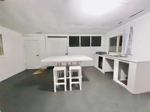 a white kitchen with a table and two stools at Private Double Room - Airport Cottage in Fua‘amotu