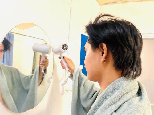 a woman blow drying her hair in front of a mirror at Comfort Hostel Phuket Old Town by MaTong in Phuket Town