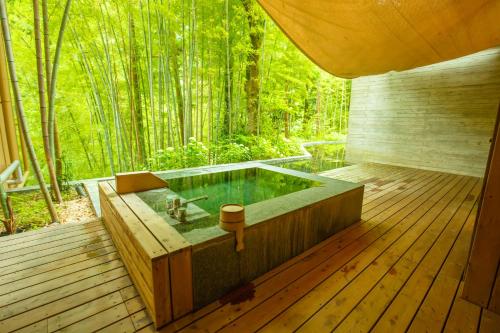 una bañera de hidromasaje en una terraza con árboles al fondo en Kinnotake Tonosawa (Adult Only) en Hakone