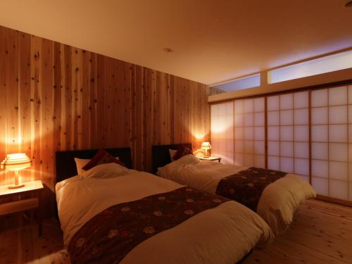 two beds in a room with wooden walls and two lamps at Hanakanzashi in Nihommatsu