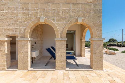 an outdoor patio with three arches and two blue chairs at Bed & Mare by Perle di Puglia in Baia Di Gallipoli