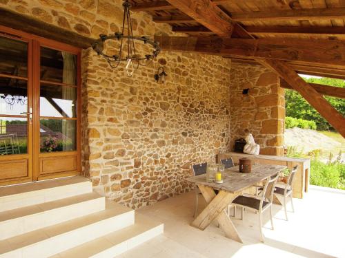 a patio with a wooden table and a stone wall at Very nice cottage with studio on a domain with heated pool in Roussines