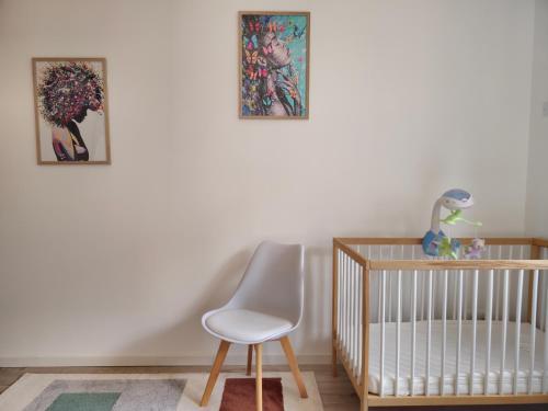 a crib and a chair in a room with two pictures at Les Quatre Baies in Guichen