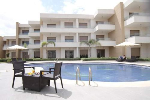 a swimming pool with two chairs and a table in front of a building at Appart luxueux Marina Saïdia Tamaris 6 piscines in Saidia 